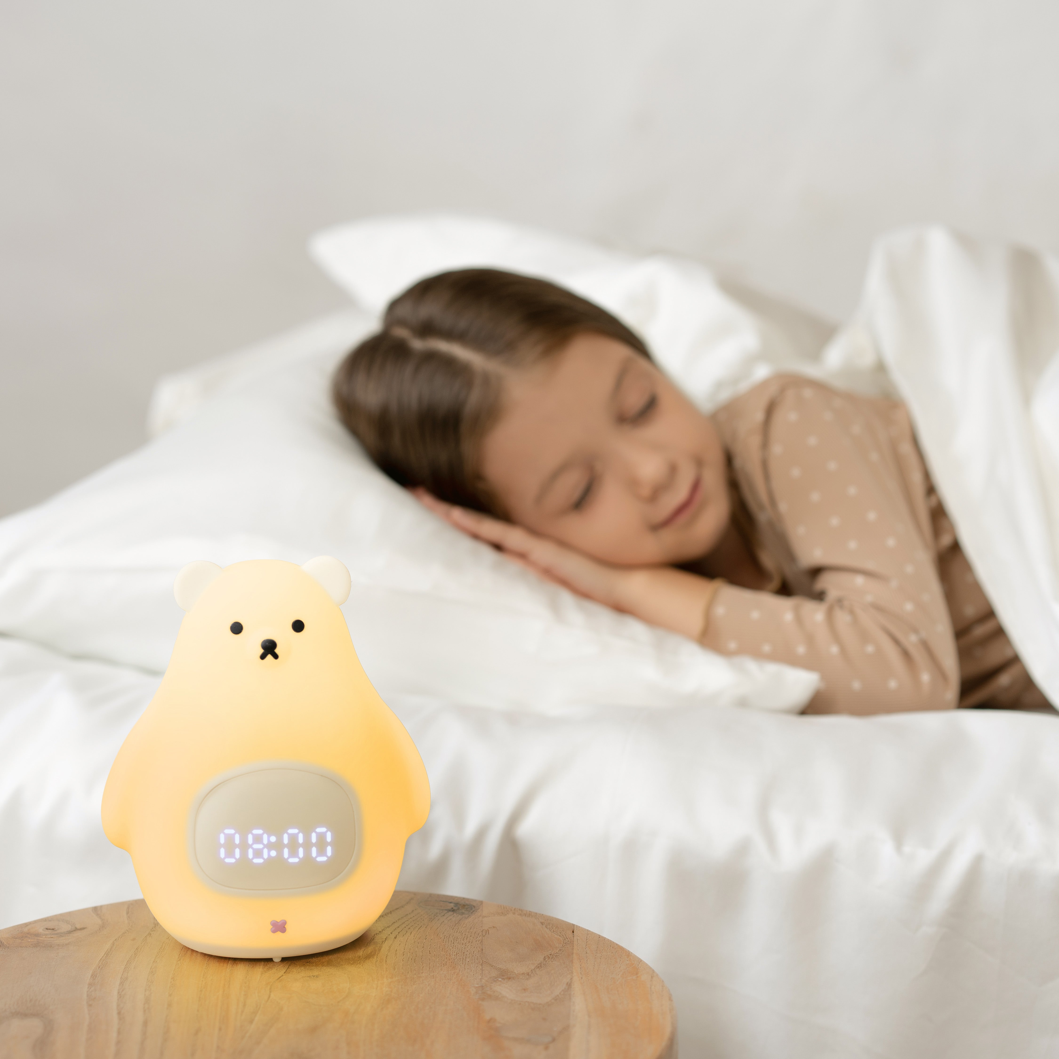 Slaaptrainer op nachtkastje met kind dat nog in bed ligt te slapen